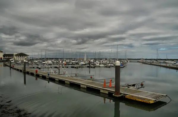  Bulutlu bir günde Dublin 'de, yelkenli ve yatlarla dolu bir limana giden uzun tahta bir dubanın geniş bir görüntüsü..
