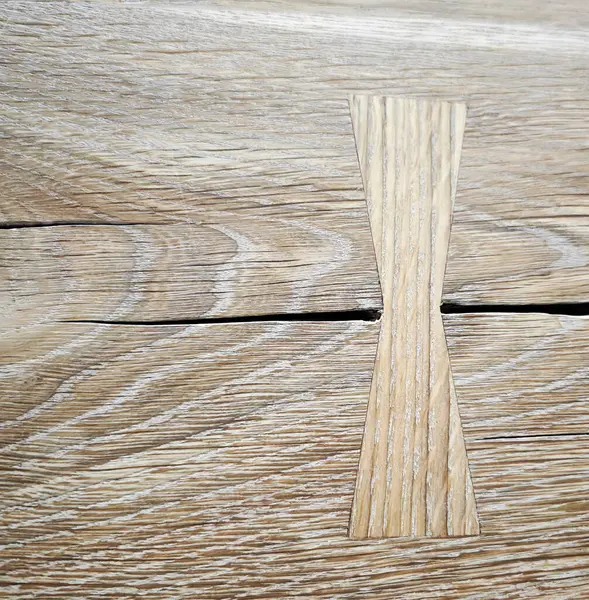 Güzel bir kelebek ya da dovetail anahtar kaplamasını gösteren yakın plan bir çekim, kırsal ahşap bir yüzeydeki doğal bir çatlağı onarmak ve güçlendirmek için ustalıkla kullanılır. Ahşabın ve doğramacılığın karmaşık tahıl desenleri geleneksel işçiliği vurguluyor..