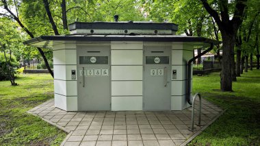 Riga 'daki tuvalet binasına ödeme yapın. Letonya, Riga 'da bir parkta, ödeme seçenekleri olan temiz ve modern bir umumi tuvaletin ön görüntüsü. Özellikler erkek, kadın ve engelli erişim sembolleri.