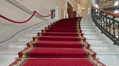 Beyaz mermer basamaklar, altın ve siyah korkuluklar ve büyük salon sonra, zengin bir kırmızı halı ile süslenmiş görkemli bir merdiven iç görünümü