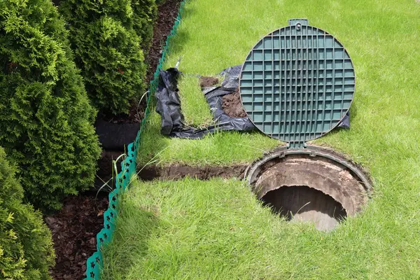 Yeşil bir çimenliğin ortasında kanalizasyon kanalını aç. Yeraltı iletişiminin tamiri. Çimenlikteki iletişimin onarılması. Özel bir evde rögar ve çimen