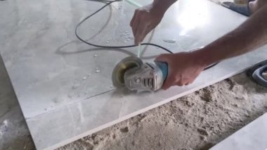Man cutting a big floor tile with an angle grinder tool. Raw footage of cutting ceramic tile with a wet saw. Water tiles grinder machine