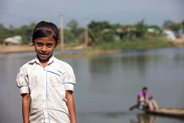 Taherpur, Bangladesh - November 05, 2019: Little girl standing in front of the river wearing a school dress. Poor school-going girl wearing a torn dress is ready to go to school.