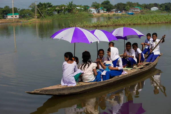 Taherpur, Bangladeş - 05 Kasım 2019: Okullu kızlar ve oğlanlar tekneyle dönüyorlar. Okul çocukları kayıkla geziyor, okul elbiseleriyle kürek çekiyor ve renkli şemsiyelerle okula gidiyor..