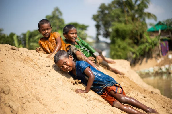 Taherpur, Bangladeş - 05 Kasım 2019: Kum tepesinde uzanan çocuğa odaklan. Bir grup çocuk ıslak elbiseler içinde nehirde banyo yapıyor ve kumlarda oynuyorlar.