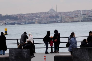 19-01-2024 İstanbul-Türkiye: İskelede İnsanlar, Bazılarının Yüzü Maskeli, Şehrin Diğer tarafında