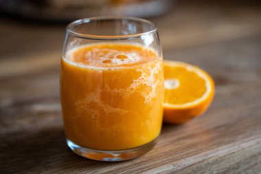 Canlı ve taze bir bardak portakal suyu hamurlu, kırsal ahşap bir masada servis edilir, sağlık ve tazelik hissi uyandırır.