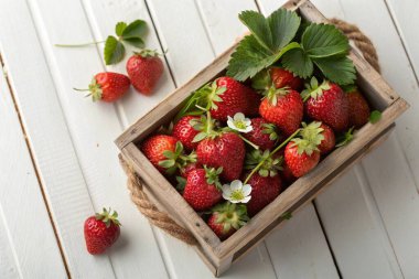 Fresh ripe strawberries in a rustic wooden crate on a white wooden table clipart