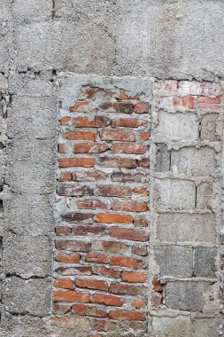 Açığa çıkmış kırmızı tuğlaları ve beton yama işi olan eski dokulu bir duvar.