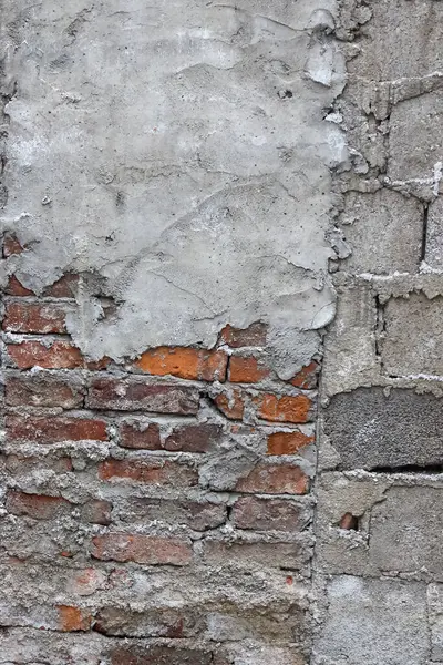 Açığa çıkmış kırmızı tuğlaları ve beton yama işi olan eski dokulu bir duvar.