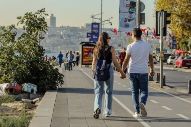 04-10-2024 İstanbul-Türkiye: Gün batımında İstanbul 'da sahil yolu boyunca el ele yürüyen çift