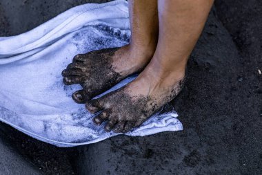 Havlunun üzerinde kadının ayakları İspanya sahilinden gelen volkanik siyah kumla kirlenmiş.
