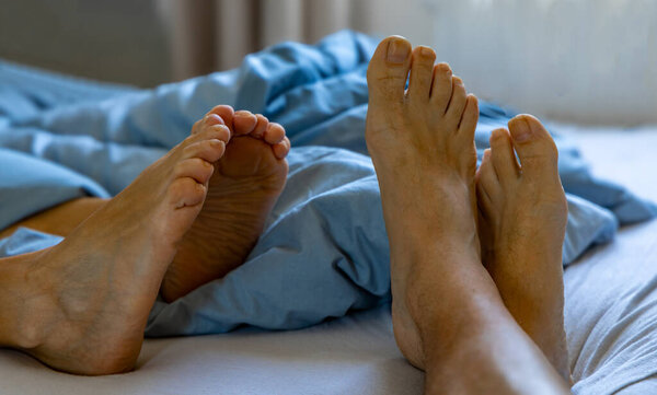 Ноги покойной женщины и мужчины на кровати на простынях