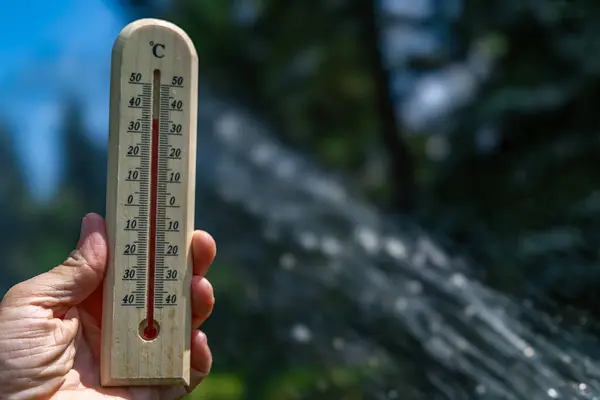 stock image A man holds a wooden thermometer in his hand in the garden which indicates a very high temperature - protection against heat