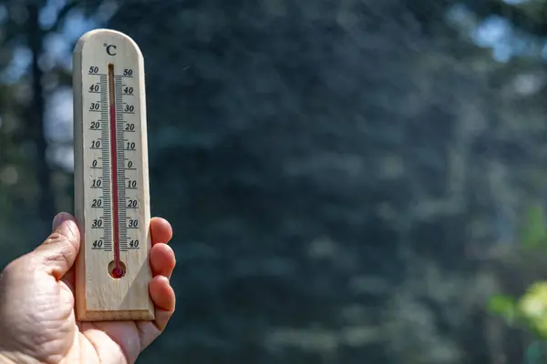 stock image A man holds a wooden thermometer in his hand in the garden which indicates a very high temperature - protection against heat