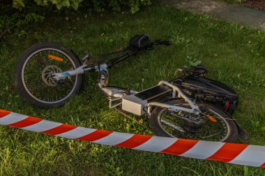 Elektrikli bisiklette bir kaza oldu. Bölge polis tarafından kırmızı ve beyaz musluklarla korunuyor.