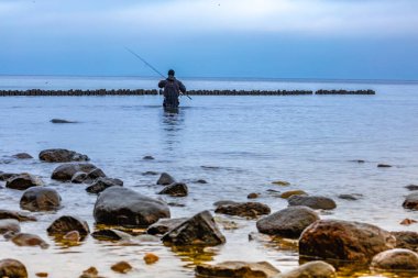Uzun botlu balıkçı, balıkçı, deniz kıyısında durur, kışın Baltık Denizi 'nde balık tutar, Gdynia, Orlow