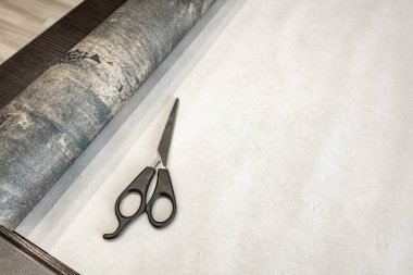 Duvara yapıştırmadan önce duvar kâğıdını, makası, bant ve kalemi kesiyor, duvar kağıdını boyuna kesiyor.