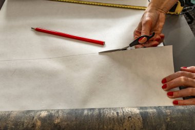 Duvara yapıştırmadan önce duvar kâğıdını, makası, bant ve kalemi kesiyor, duvar kağıdını boyuna kesiyor.