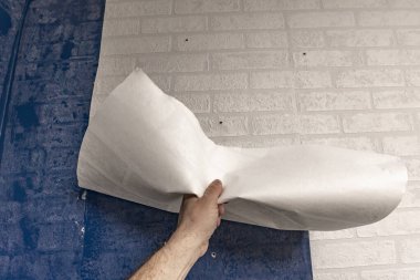 Yatak odasındaki duvardan eski duvar kağıtlarını sökmek, apartman tadilatı, evdeki duvar kağıtlarını yenilemek, duvara plastik duvar kağıdı yapıştırmak.