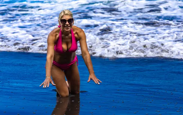 Tenerife 'de plajda dinlenirken, Atlantik Okyanusu' nda yıkanan bir kadın, güneş banyosu yapan bir kadının vücudunda siyah volkanik kum.