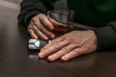 Sarhoş bir adam elinde bir bardak alkol ve arabanın anahtarıyla masada yatıyordu.