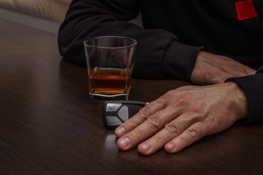 Sarhoş bir adam elinde bir bardak alkol ve arabanın anahtarıyla masada yatıyordu.