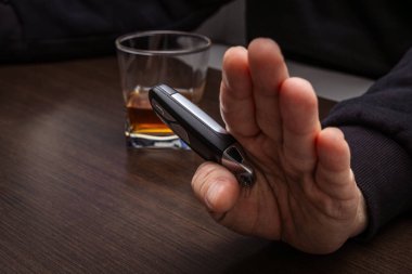 Sarhoş bir adam elinde bir bardak alkol ve arabanın anahtarıyla masada yatıyordu.