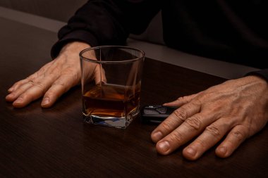 Sarhoş bir adam elinde bir bardak alkol ve arabanın anahtarıyla masada yatıyordu.