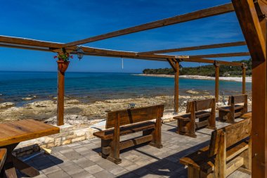 Hırvatistan 'da Adriyatik Denizi kıyısında güneşten korunan boş bank, tahta pergola, mevsimden önce kahve ve soğuk içeceklerle dolu küçük bir bar