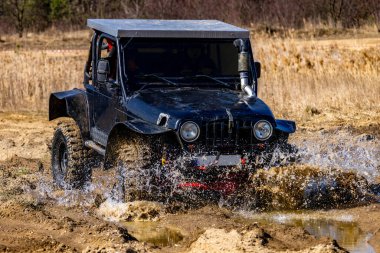 Şehir dışındaki arazi testinde siyah off-road aracı, off-road aracıyla su dolu bir hendeği geçiyor.