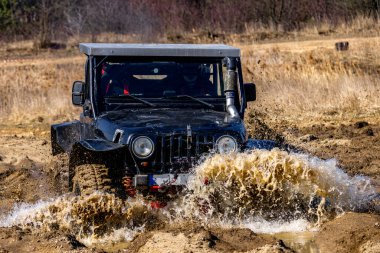Şehir dışındaki arazi testinde siyah off-road aracı, off-road aracıyla su dolu bir hendeği geçiyor.
