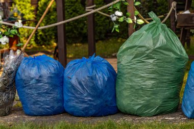 Bahçeyi temizliyor, çimenleri ve çöpleri tırmıklıyor, çimenleri çöp dolu poşetlerle dolduruyor, bahçeyle uğraşıyor.