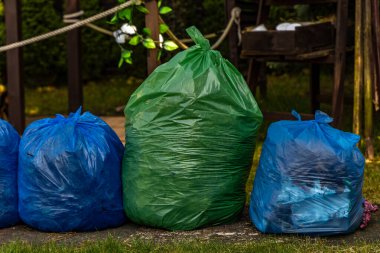 Bahçeyi temizliyor, çimenleri ve çöpleri tırmıklıyor, çimenleri çöp dolu poşetlerle dolduruyor, bahçeyle uğraşıyor.