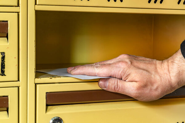 Желтые почтовые ящики на лестничной клетке многоквартирного дома, раздача рекламных листовок, а почтальон кладет письма в почтовый ящик