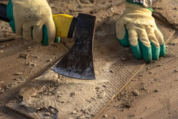 Eldivenli kadın beton zemini baltayla parçalıyor, fayansları temizliyor, döşemeleri söküyor, fayansları terrac 'a seriyor.