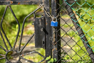 Küçük mavi bir asma kilit, metal bir çitte asılı bir anahtar, kapalı bir bahçe silahı.