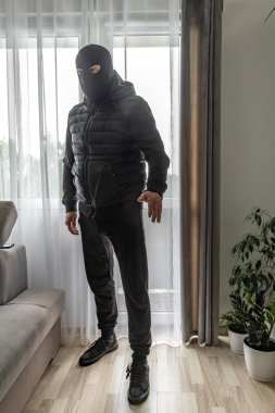 Kar maskeli bir hırsız balkondan bir daireye giriyor, suçlu pencereden eve giriyor.