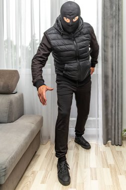 Kar maskeli bir hırsız balkondan bir daireye giriyor, suçlu pencereden eve giriyor.