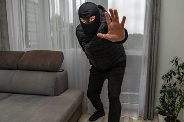 Kar maskeli bir hırsız balkondan bir daireye giriyor, suçlu pencereden eve giriyor.