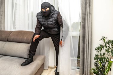 Kar maskeli bir hırsız balkondan bir daireye giriyor, suçlu pencereden eve giriyor.