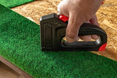 Yapay çimenleri ve yapay sarmaşık yapraklarını çivileyerek tahta bir tahtaya raptiye ve metal zımbalarla çivileyerek eski bir kapıyı yeniliyordu.