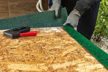 Yapay çimenleri ve yapay sarmaşık yapraklarını çivileyerek tahta bir tahtaya raptiye ve metal zımbalarla çivileyerek eski bir kapıyı yeniliyordu.