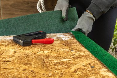 Yapay çimenleri ve yapay sarmaşık yapraklarını çivileyerek tahta bir tahtaya raptiye ve metal zımbalarla çivileyerek eski bir kapıyı yeniliyordu.