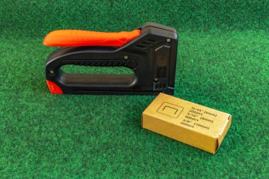 Yapay çimenleri ve yapay sarmaşık yapraklarını çivileyerek tahta bir tahtaya raptiye ve metal zımbalarla çivileyerek eski bir kapıyı yeniliyordu.