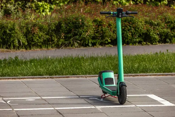 Şehir merkezindeki kaldırımın ortasına park edilmiş yeşil scooter, yanlış park edilmiş elektrikli scooter.