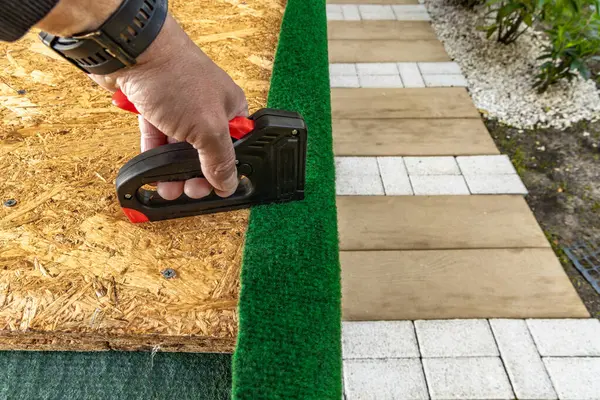 Yapay çimenleri ve yapay sarmaşık yapraklarını çivileyerek tahta bir tahtaya raptiye ve metal zımbalarla çivileyerek eski bir kapıyı yeniliyordu.