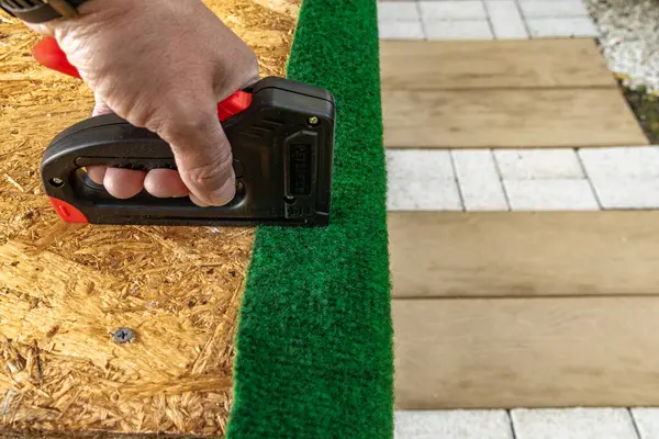 Yapay çimenleri ve yapay sarmaşık yapraklarını çivileyerek tahta bir tahtaya raptiye ve metal zımbalarla çivileyerek eski bir kapıyı yeniliyordu.