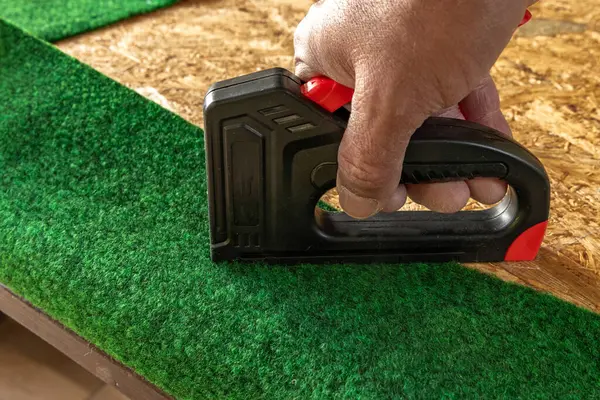 Yapay çimenleri ve yapay sarmaşık yapraklarını çivileyerek tahta bir tahtaya raptiye ve metal zımbalarla çivileyerek eski bir kapıyı yeniliyordu.