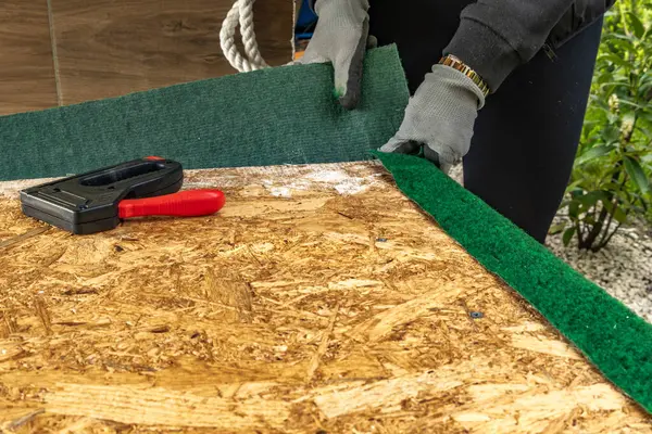 Yapay çimenleri ve yapay sarmaşık yapraklarını çivileyerek tahta bir tahtaya raptiye ve metal zımbalarla çivileyerek eski bir kapıyı yeniliyordu.